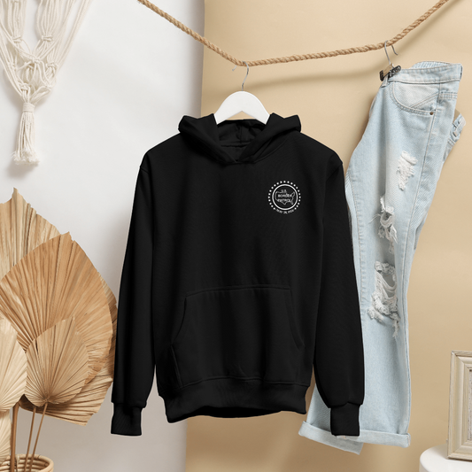 Black hoodie with a logo on a hanger next to light blue jeans against a neutral wall.